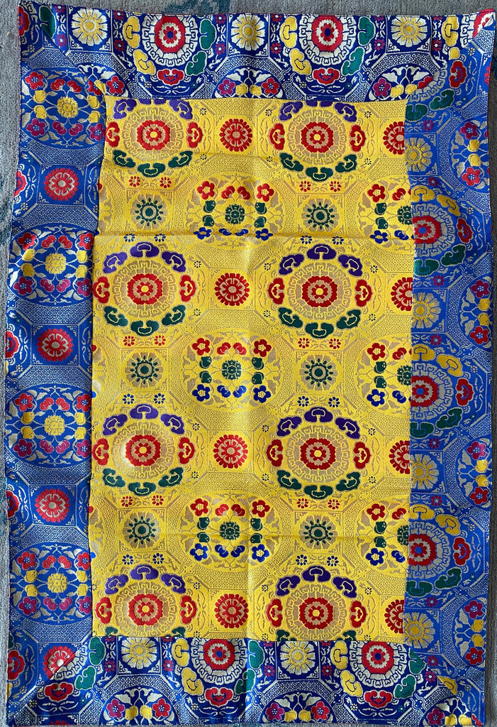 Rectangular Tibetan brocade with blue border with a yellow base covered in red, green, and blue traditional Tibetan flower designs.