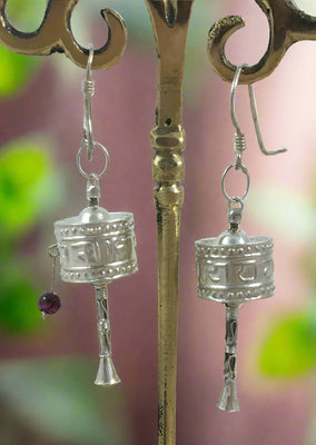 A pair of sterling silver prayer wheel earrings with hook style pierced earrings, displayed against a backdrop of crystal stones.
