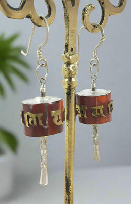 A pair of silver prayer wheel earrings with red and gold accents, featuring inscription in Devanagari script.